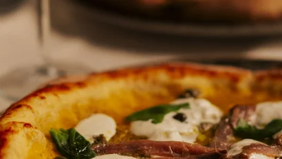 Pizza con mozzarella, acciughe e basilico accanto a un bicchiere di vino bianco