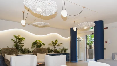 Sala d'attesa moderna con poltrone bianche, piante e luci decorative al soffitto