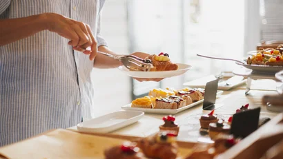 Persona che prende un dolce da un buffet di pasticceria con pinze