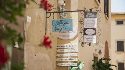 Insegne di negozi tipici toscani appese a un muro in una strada di paese