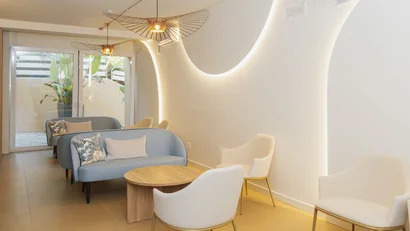 Salotto moderno con poltrone beige e divani blu, illuminazione a parete curva.