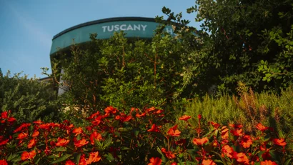 Fiori rossi davanti a un edificio con scritta Tuscany sotto un cielo blu