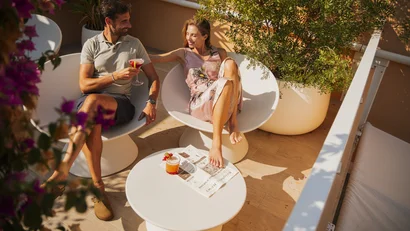 Coppia che si rilassa con cocktail su terrazza soleggiata con piante