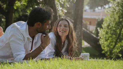 Coppia sdraiata sull'erba che conversa in un parco soleggiato