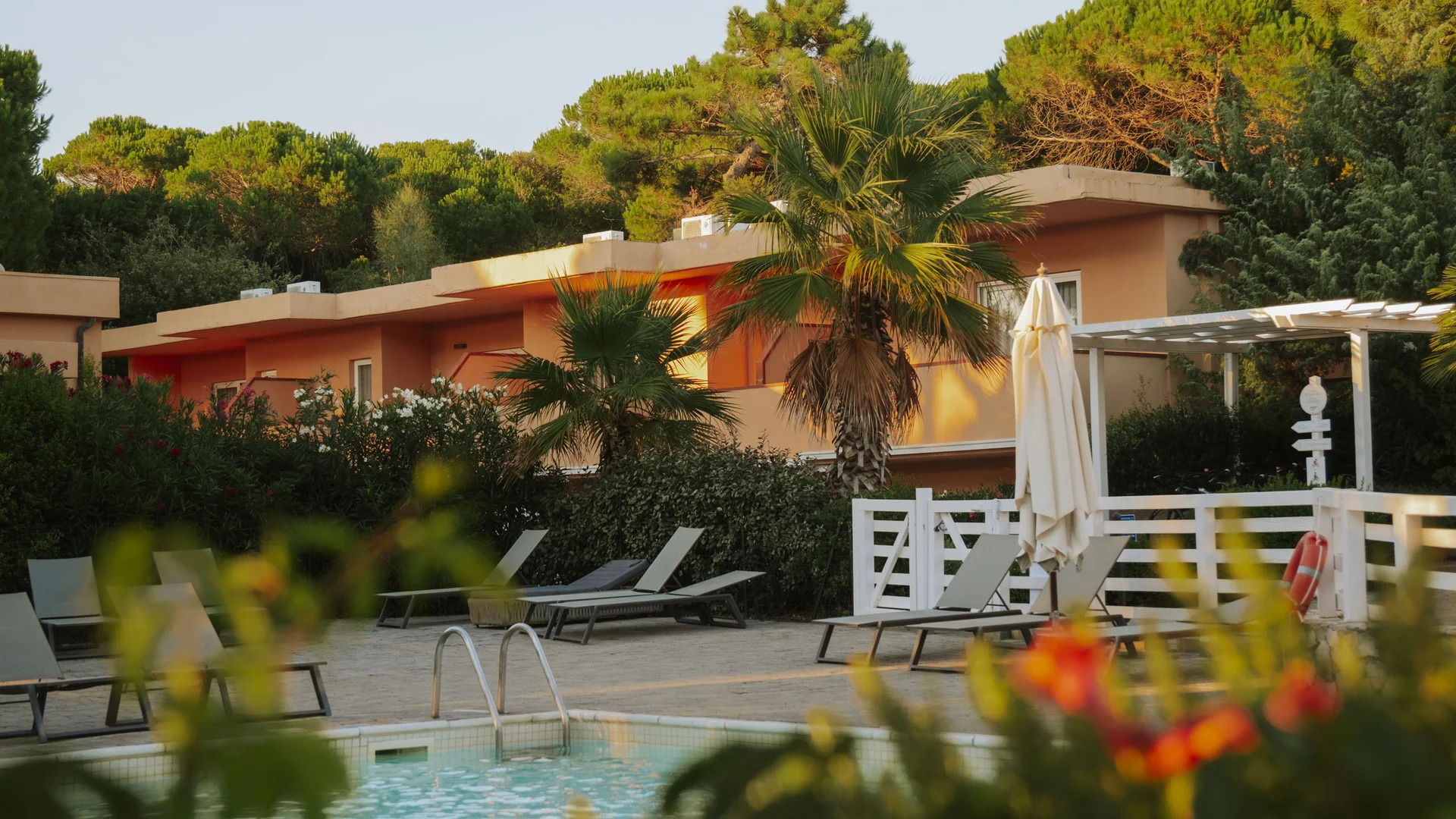 Piscina con sedie a sdraio e vegetazione davanti a una casa arancione