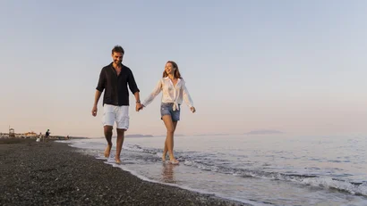 Coppia felice che cammina a piedi nudi sulla spiaggia al tramonto