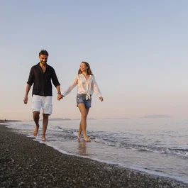Coppia felice che cammina a piedi nudi sulla spiaggia al tramonto