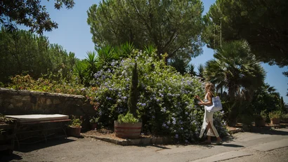 Donna che cammina vicino a cespuglio fiorito in giardino soleggiato.